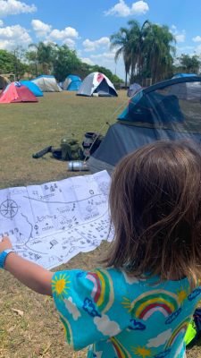 menina de costas segurando um mapa em um camping cheio de barracas